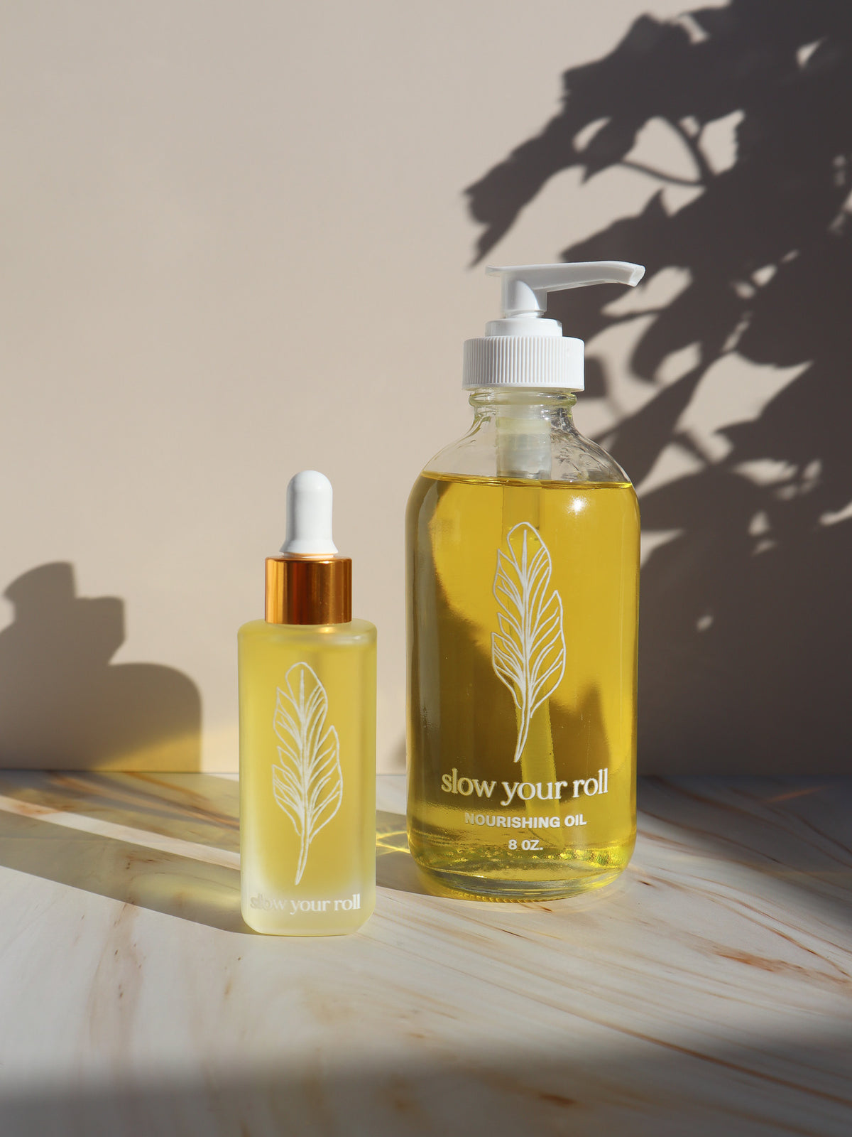 Slow Your Roll Nourishing Oil 8 oz back bar pump bottle next to the 1 oz retail dropper for size comparison